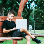 Boy_with_using_laptop_on_the_swing._First_time_to_school._Outdoor_learning_concept._Vintage_color_filter